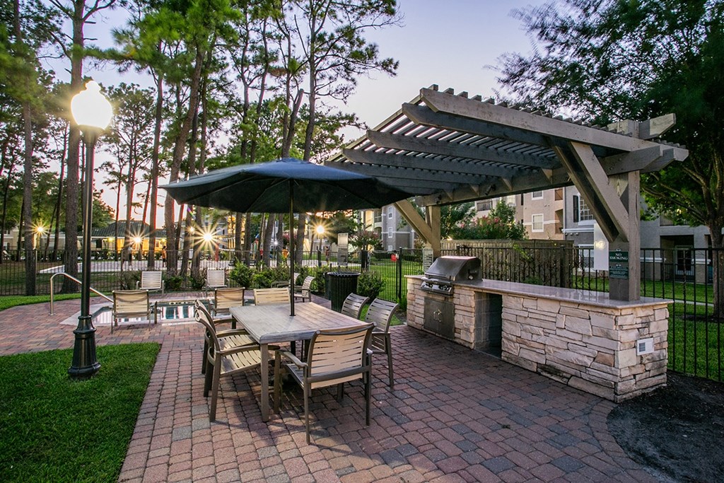 a patio with a grill and a table with chairs and umbrellas