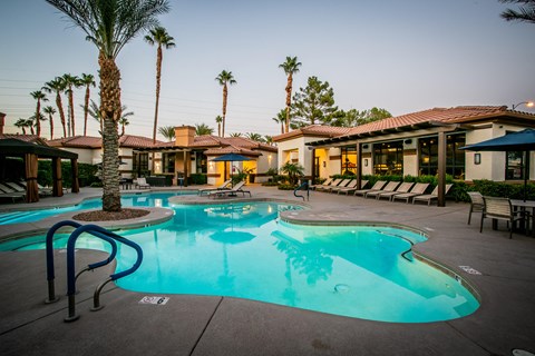 a large swimming pool with palm trees and a building in the background
