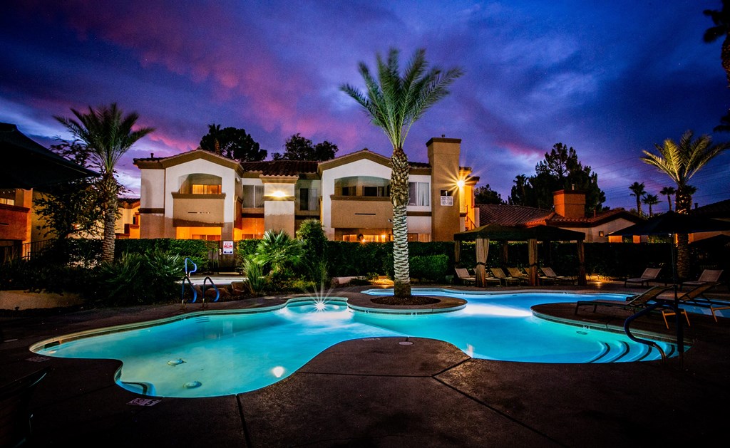 a swimming pool at night at an apartment complex with palm trees