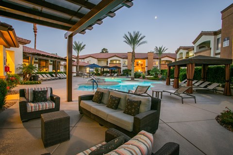 a patio with couches and chairs around a pool at night