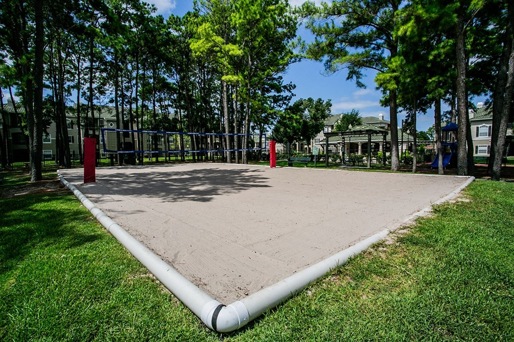 a sand volleyball court sits in the middle of a grassy area