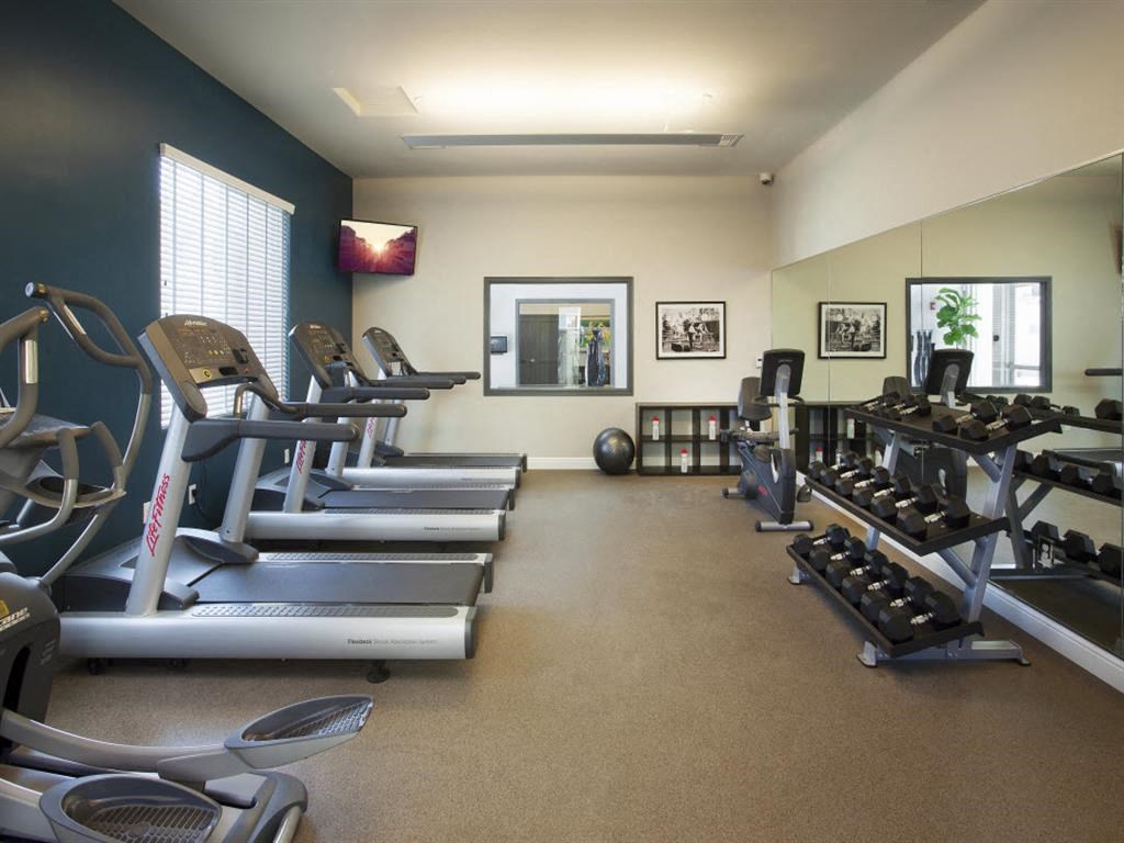 Apartments in Santa Maria, CA for Rent - Hancock Terrace - 24-Hour Fitness Center with Cardio Equipment, Free Weights, TV, Large Window, and Mirror Wall.