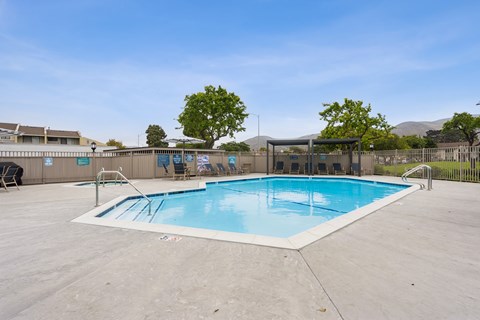 Lompoc, CA, Apartments - Oceanwood Apartments - A Large Outdoor Swimming Pool Features A Wide Concrete Deck, Metal Handrails, Lounge Seating Under Shade Structures, And A Fenced Perimeter.