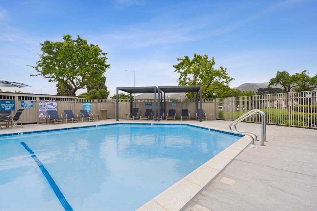 A large outdoor swimming pool with a blue tiled edge and a metal fence surrounding it.