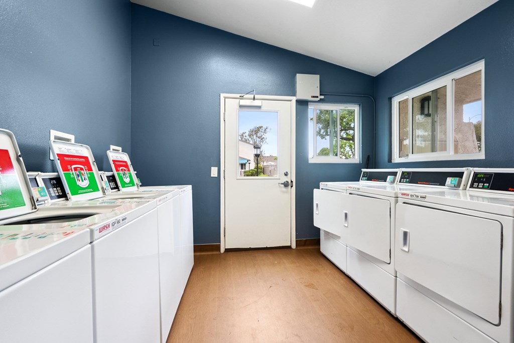 A laundromat with washers and dryers and a view of the outside.