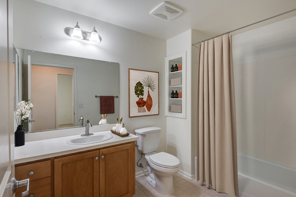 Santa Maria, CA Apartments - Hancock Terrace - Bathroom with Built-In Shelving, Spacious Vanity with Sink and Mirror, and Garden-Style Tub Shower.