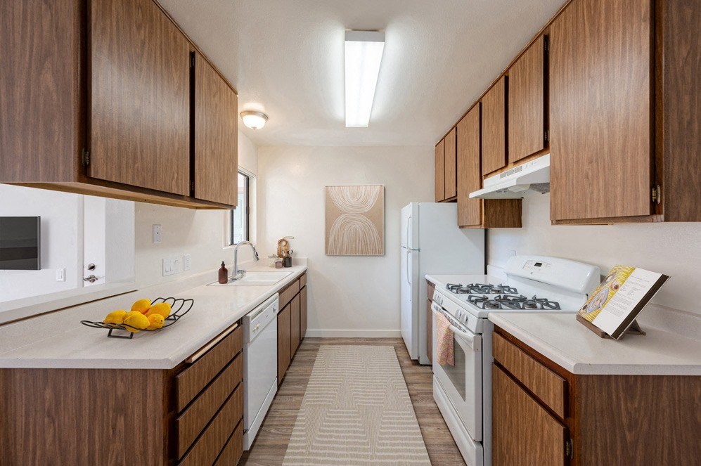 Santa Maria, CA Apartments - Knollwood Meadows - Aisle-Style Kitchen with Wood-Patterned Cabinetry, White Appliances, and White Countertops