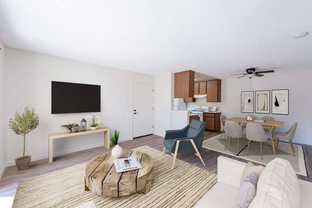 Santa Maria, CA Apartments Near Target - Knollwood Meadows - Living Room With Wood-Style Flooring, Area Rug, Sectional Sofa, Armchair, Round Wooden Coffee Table, Wall-Mounted TV, And View Of Dining Area And Kitchen.