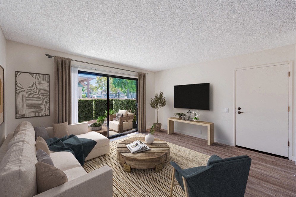 Apartments for Rent in Santa Maria, CA - Knollwood Meadows - Living Room With Wood-Style Flooring, Area Rug, Sectional Sofa, Armchair, Round Wooden Coffee Table, Wall-Mounted TV, And Sliding Glass Door With Access To Patio.