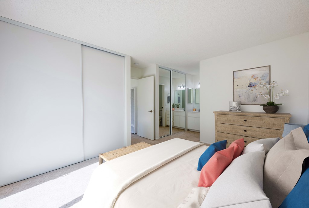 Apartments in Lompoc, CA for Rent - Oceanwood - Bedroom with Mirror Sliding Closet Doors, an Ottoman, and Colorful Pillows