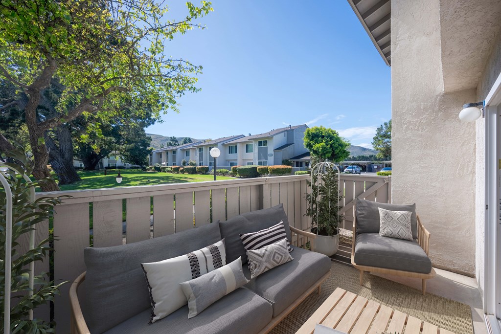A balcony with a grey couch and pillows overlooking a building.