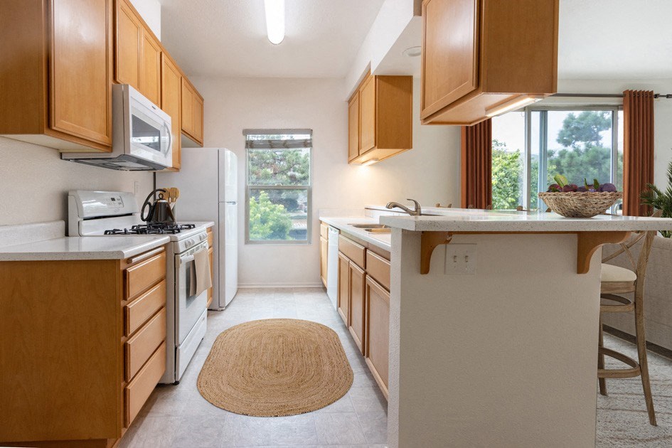 One-Bedroom Apartments in Lompoc, CA - Oceanwood - Kitchen with Refrigerator, Gas Range, Microwave Oven, Wood Cabinets, Breakfast Bar, and Bar-Style Chairs.