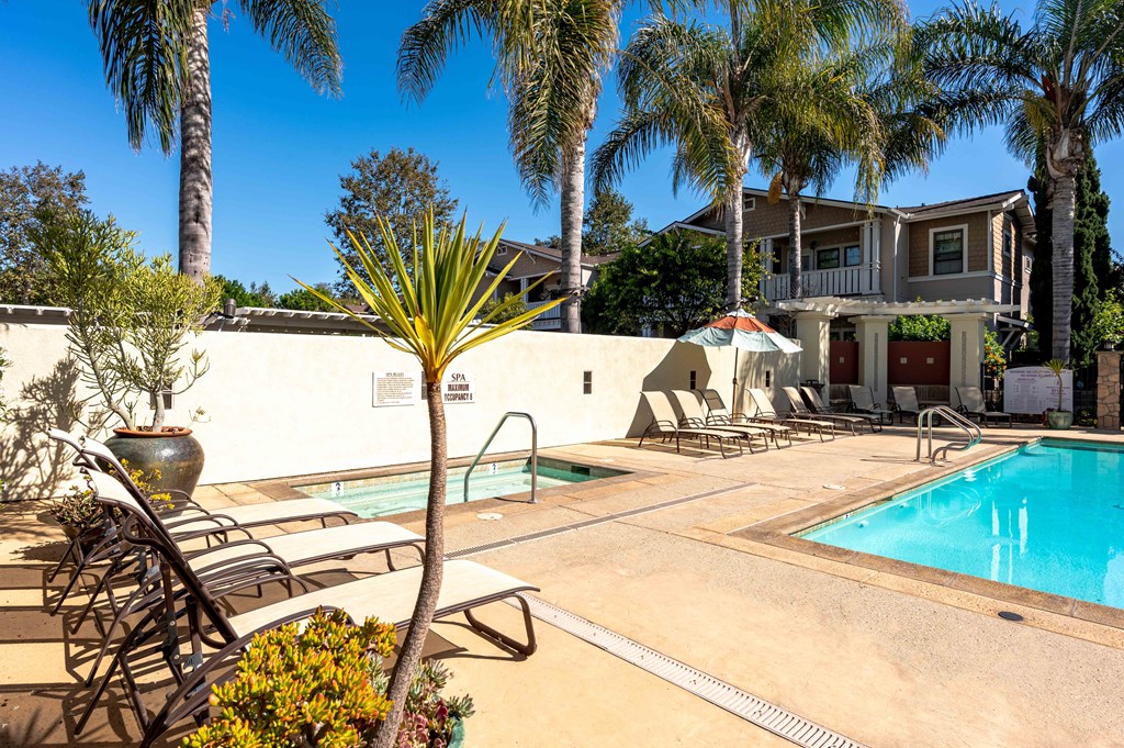 a swimming pool with chairs and palm trees in front of a house