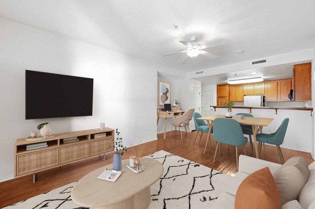 Apartments In Ventura, CA For Rent - Ralston Courtyards - Living Room With Plank Flooring, Area Rug, Couch, Coffee Table, Media Cabinet, Wall-Mounted TV, Ceiling Fan, And View Of Dining Area And Kitchen.