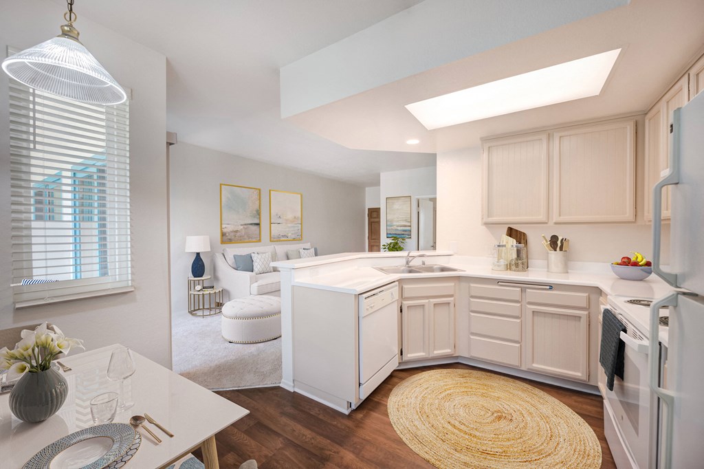 One-Bedroom Apartments in Santa Barbara, CA - Rancho Franciscan - Kitchen with Wood-Style Flooring, Bright Lighting, White Appliances, Dining Table, and View of Living Area.