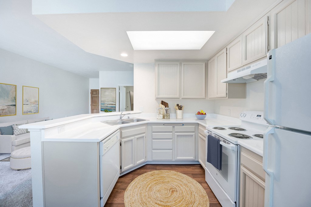 Assisted Living in Santa Barbara, CA - Rancho Franciscan - Kitchen With White Cabinetry, White Appliances, White Countertops, Flush Mount Light Fixture, and Round Natural Woven Rug
