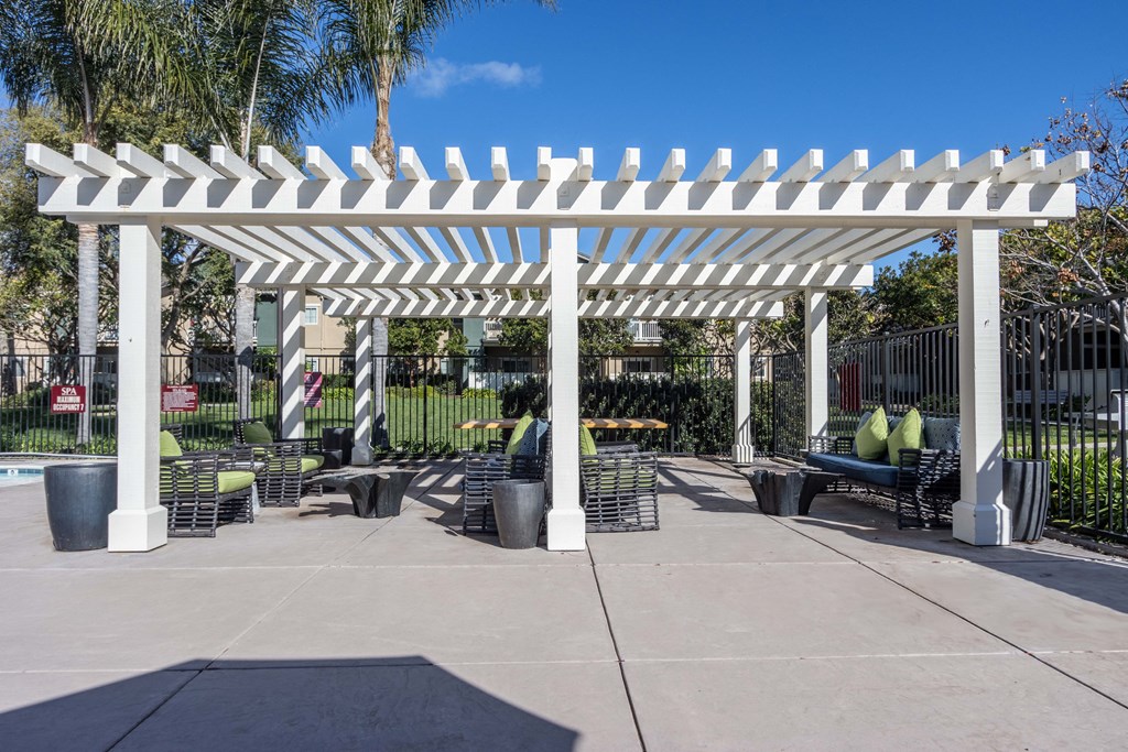 a white pergola with benches and chairs under it on a sidewalk