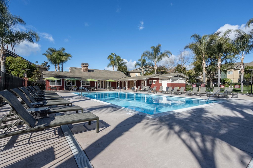 3 BR Apartments in Goleta CA - Sumida Gardens - Gated Sparkling Pool with Lounge Chairs, Green Umbrellas, and View of Clubhouse and Nearby Palm Trees
