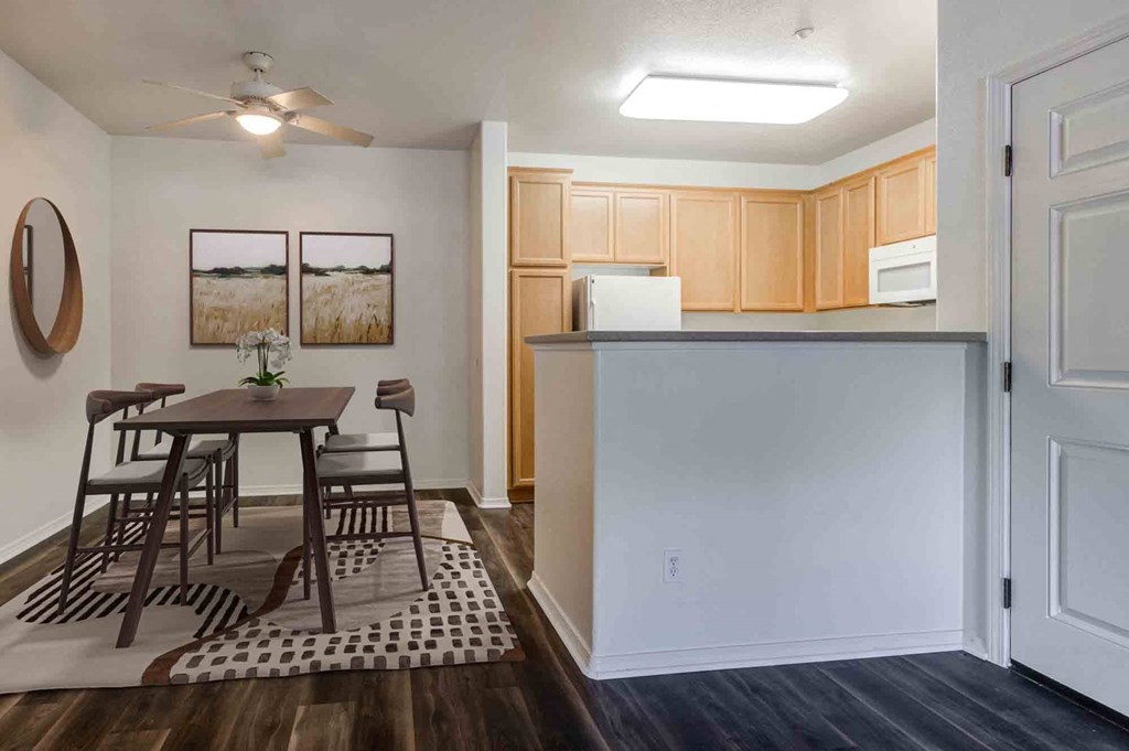 Pet-Friendly Apartments in Goleta, CA - Sumida Gardens - Dining Area with Wood-Style Flooring, Area Rug, Table and Chairs, Ceiling Fan, and View of Kitchen.