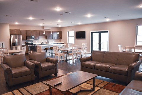 A living room with brown leather furniture and a kitchen in the background.
