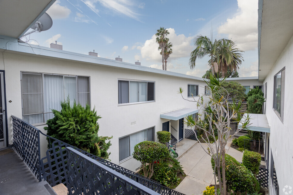 a balcony with a black railing and a white building with palm trees in the background