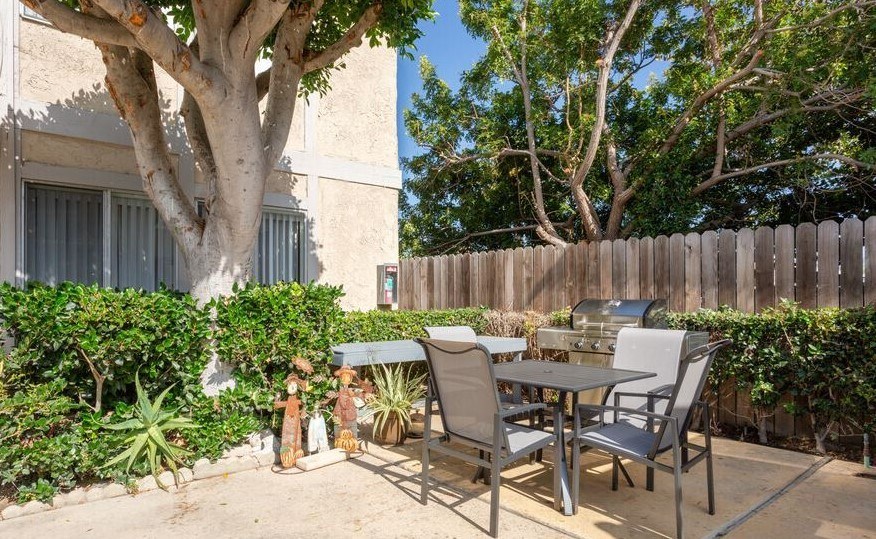 A patio with a table and chairs surrounded by greenery and a fence.