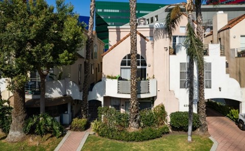 A white building with a balcony is surrounded by greenery.