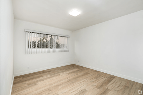 a living room with white walls and wood floors and a window
