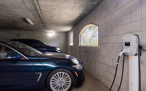A blue car is parked in a parking garage and charging its battery.