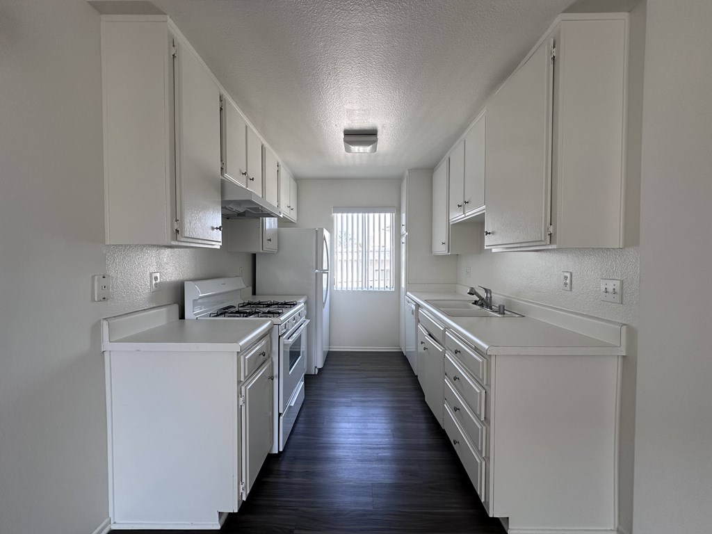 A long white kitchen with black floors and white appliances.