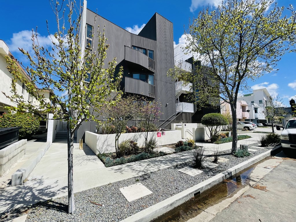 A modern building with a grey facade is surrounded by a garden with a small pond.