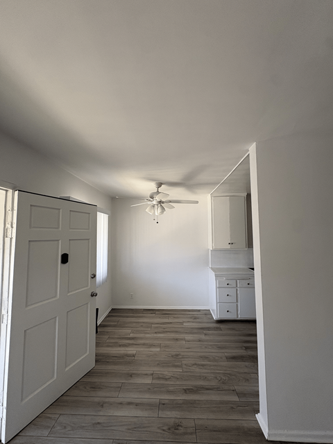A white door is open to a room with a ceiling fan.