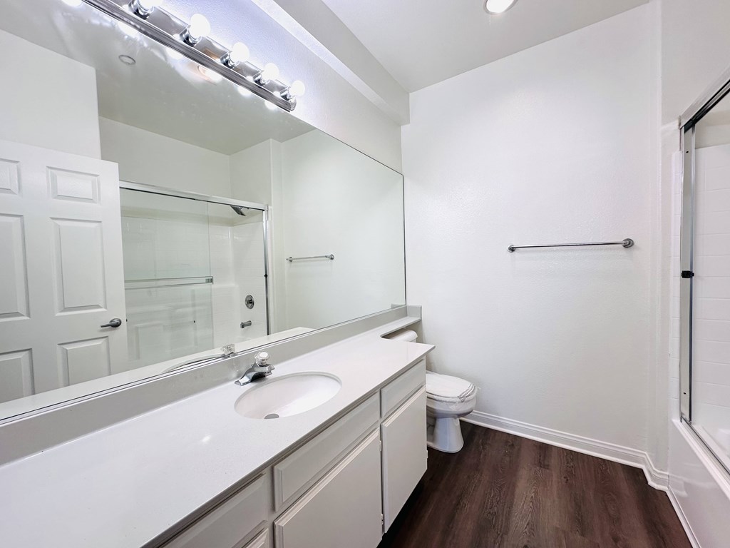 A white bathroom with a toilet, sink, mirror, and lights.