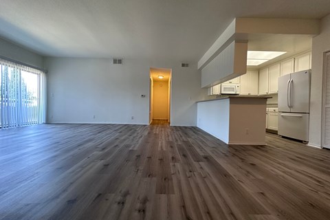 A room with wooden flooring and a kitchen area in the background.
