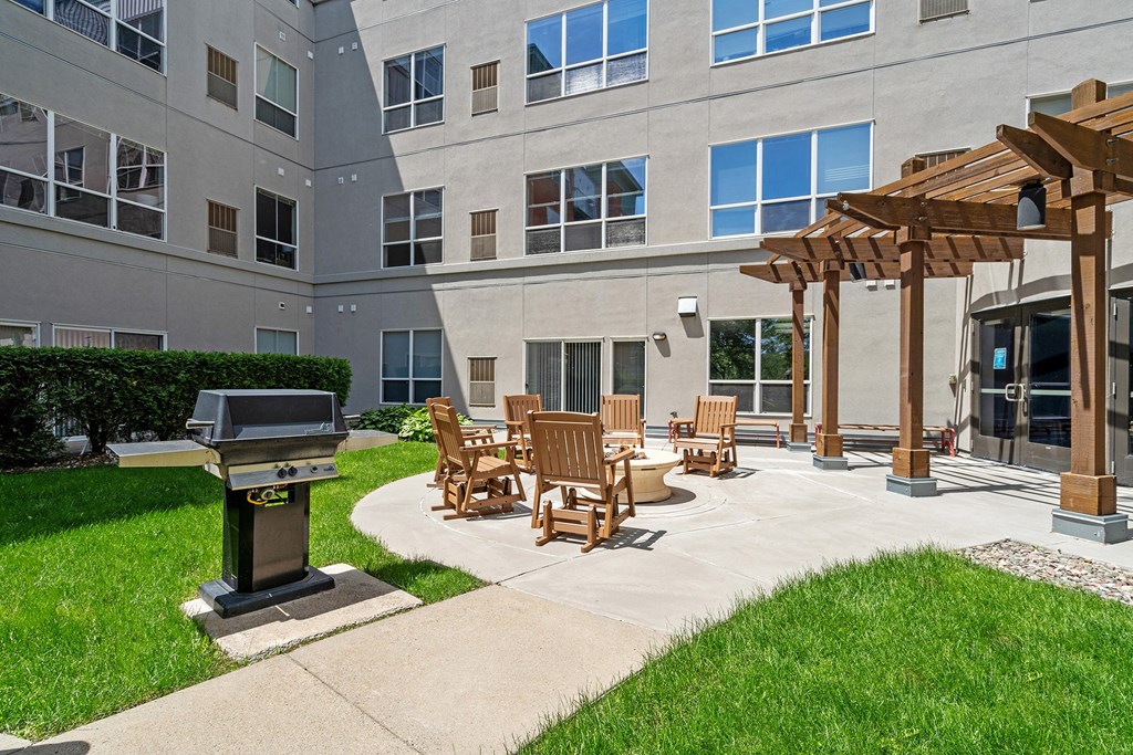 an outdoor patio with a grill and chairs in front of an apartment building
