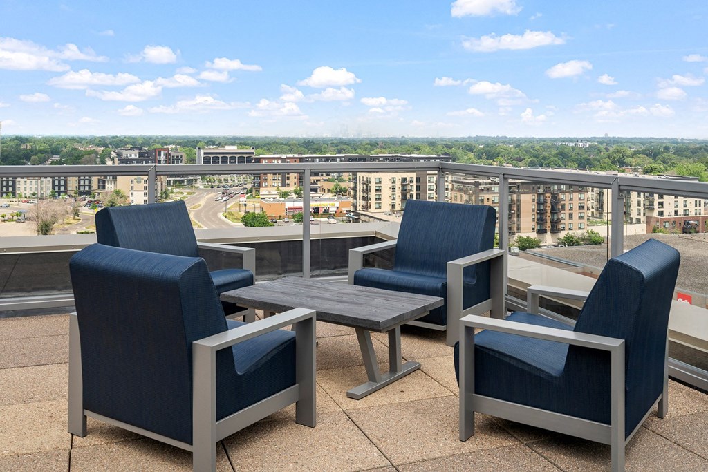 an outdoor patio with blue chairs and a wooden table with a view of the city