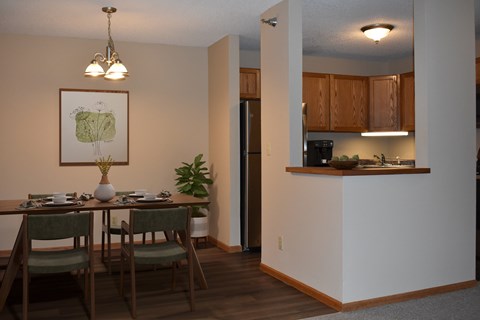 A dining room with a table set for two and a kitchen area in the background.
