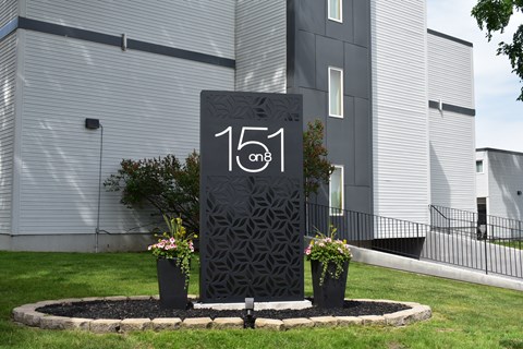 A black sign with the number 151 on it is in the foreground of a building.