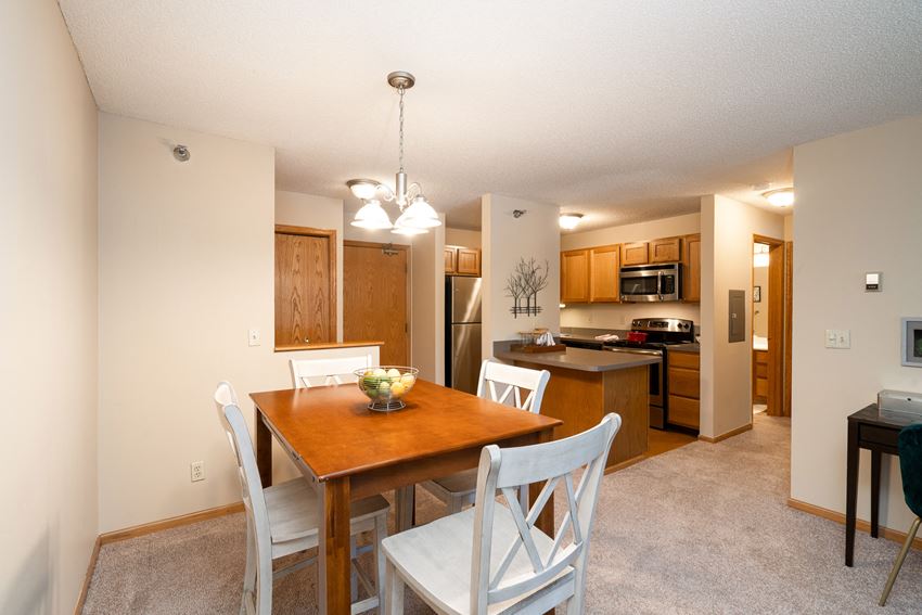 Kitchen and dining room with white chairs, wooden table, and a bright hanging lamp