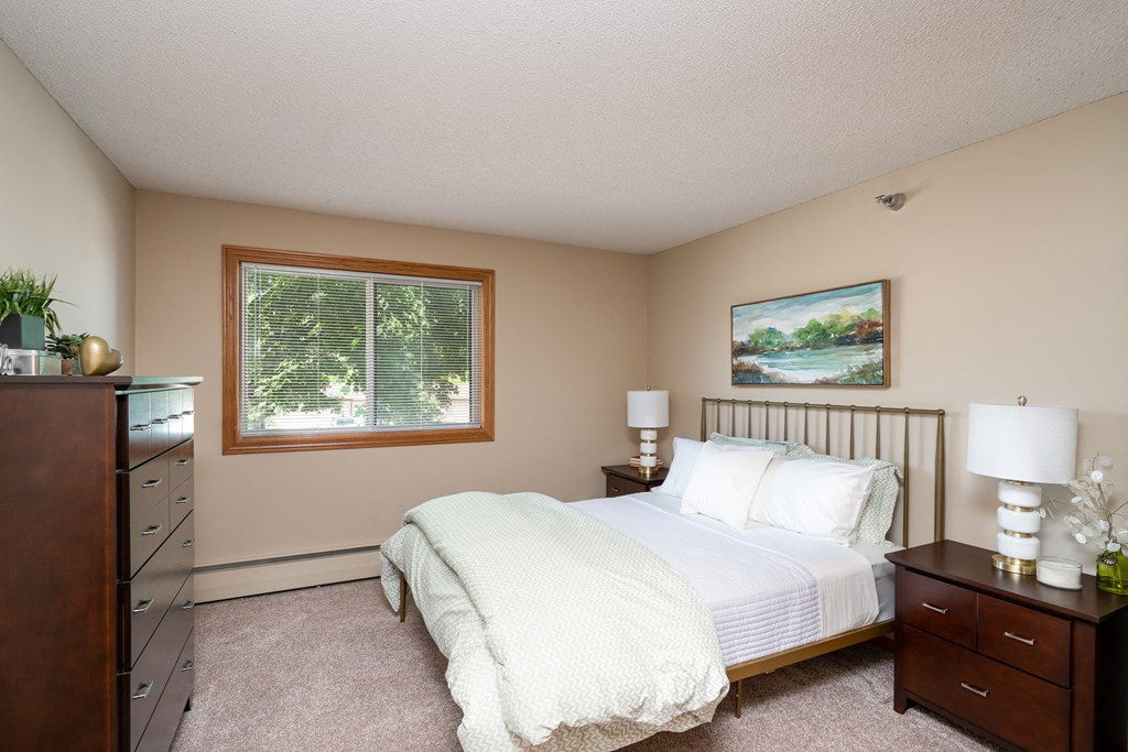 Bedroom with white comforter, and a lamp on the wooden nightstand