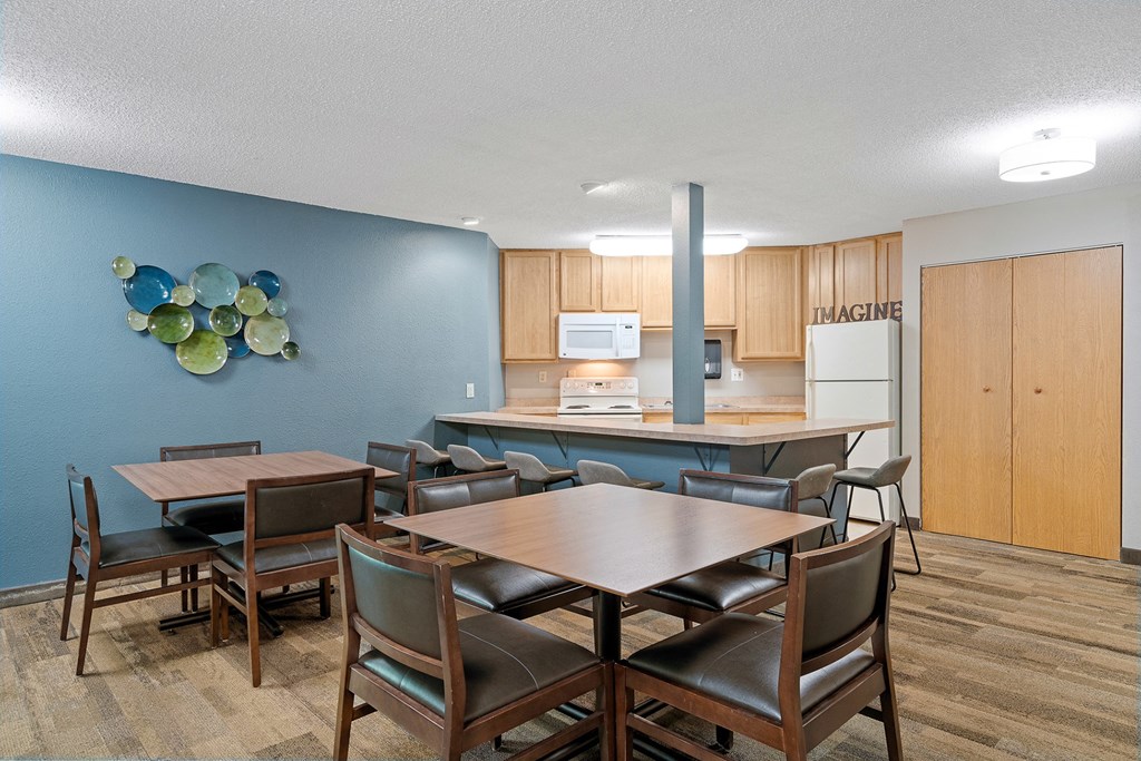 a room with a table and chairs and a kitchen in the background