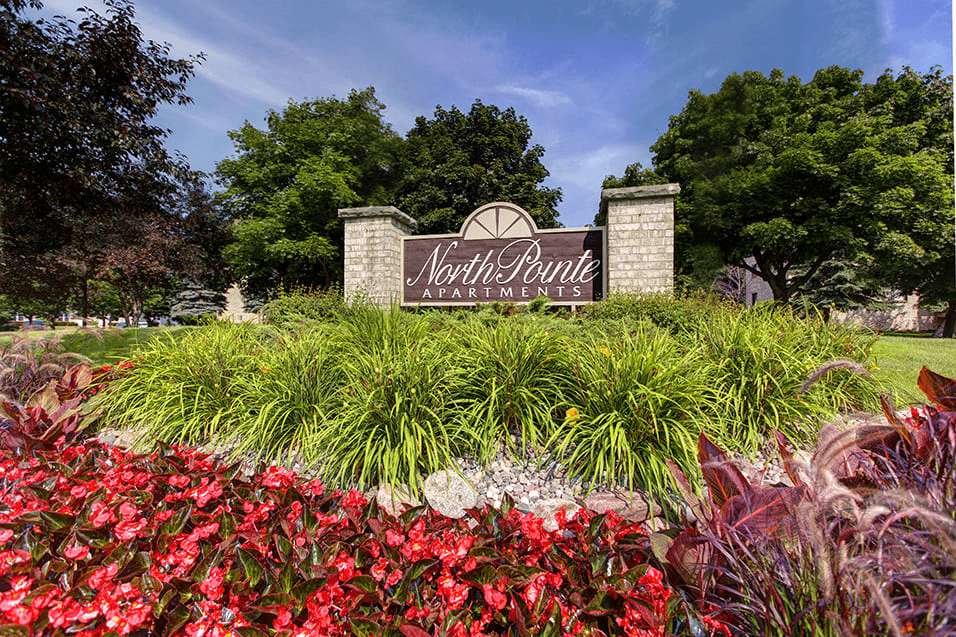 A sign for North Point Apartments is surrounded by flowers and greenery.