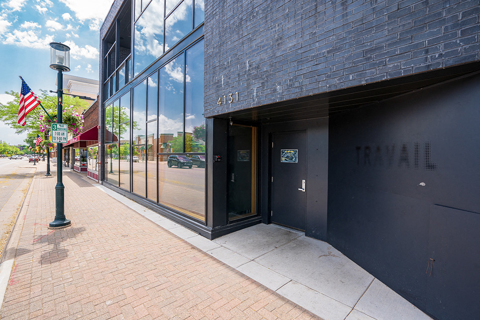 A black storefront with tinted windows and a black door, with the word "TRAVAIL" written in a different shade of black
