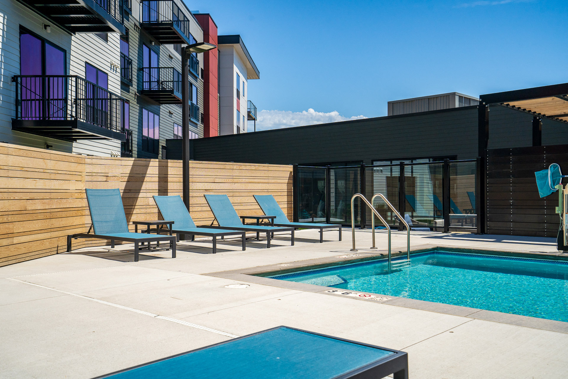 Pool and pool chairs next to apartment units' balconies and a blue sky