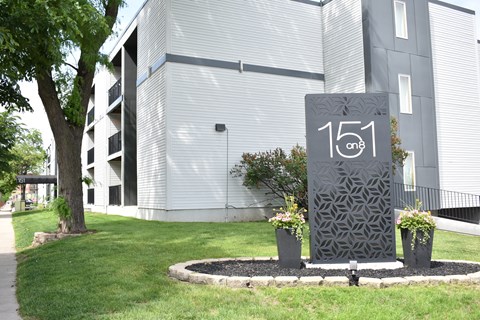 A grey sign with the number 151 on it in front of a building.