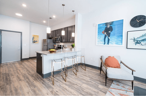 A kitchen with a bar and a chair with an orange pillow.
