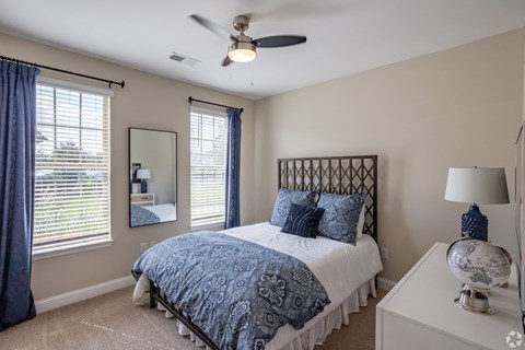 A bedroom with a bed, a ceiling fan, and a nightstand with a lamp.