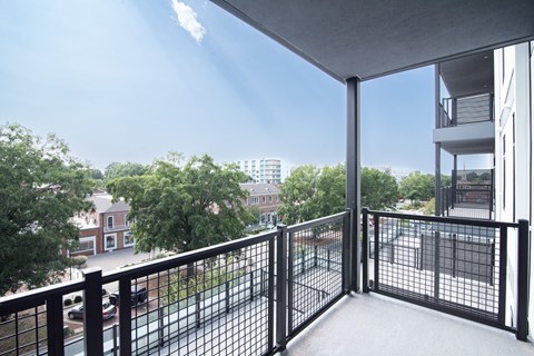 A balcony with a black railing overlooks a parking lot and buildings.