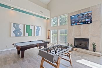 A pool table with a television above it in a room with a fireplace at The Falls Apartments in Raleigh NC