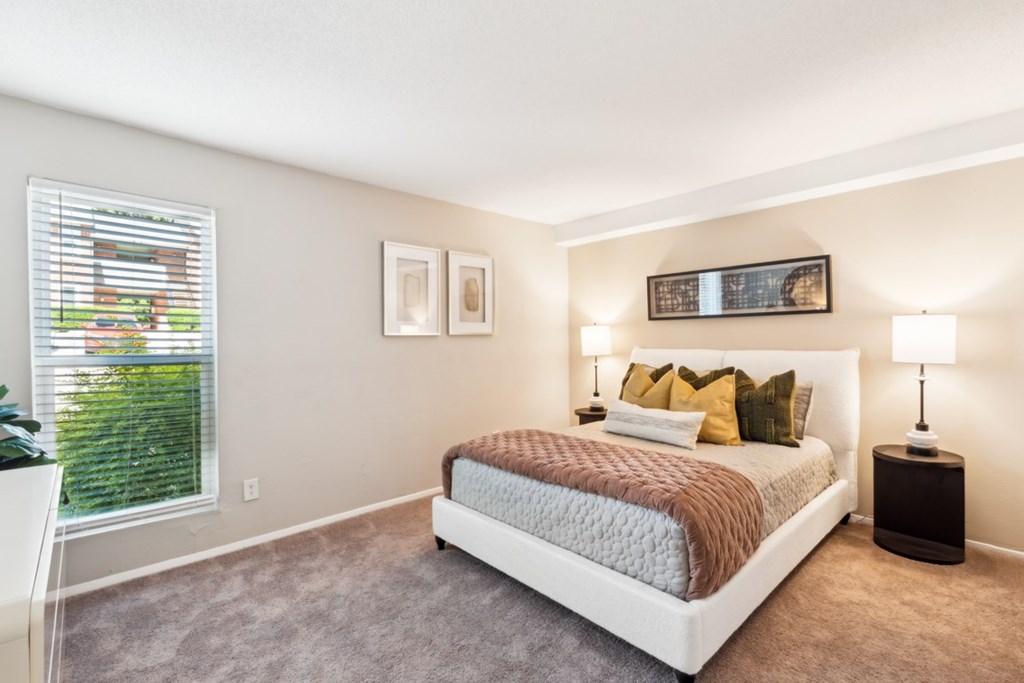 A bedroom with a large bed and a window with blinds. at Woodcreek Apartments, Cary, NC